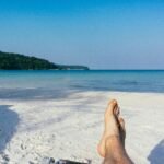 a person laying on a beach with their feet in the sand